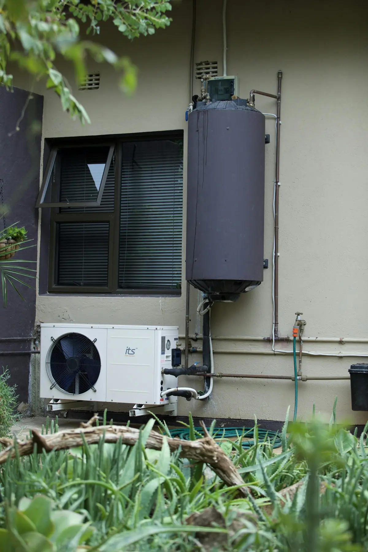 Depósito de agua caliente y unidad de bomba de calor instalados junto a una vivienda